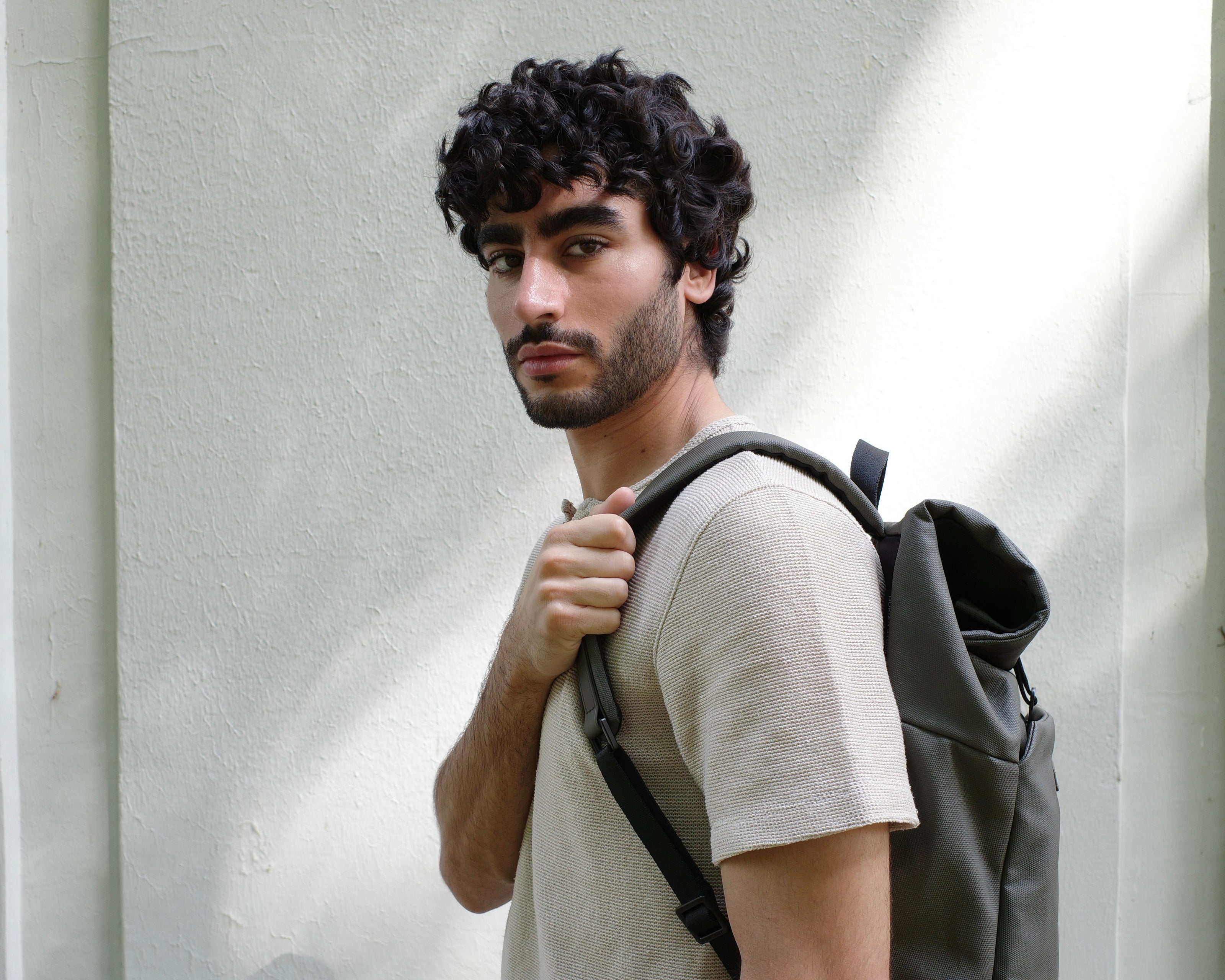 Man with a backpack standing against a light-colored wall