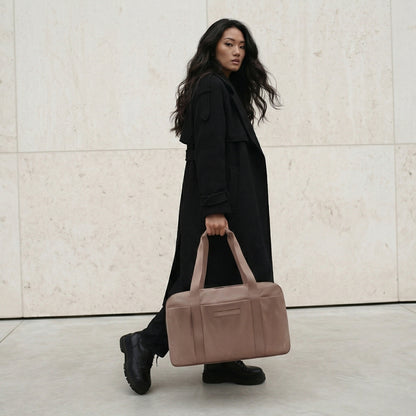 Woman holding a brown bag against a light-colored wall